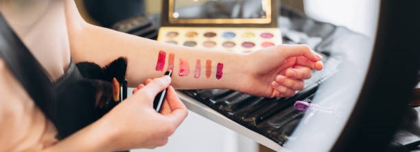 A woman carefully applies bright red lipstick to check shades, showcasing her beauty and confidence.