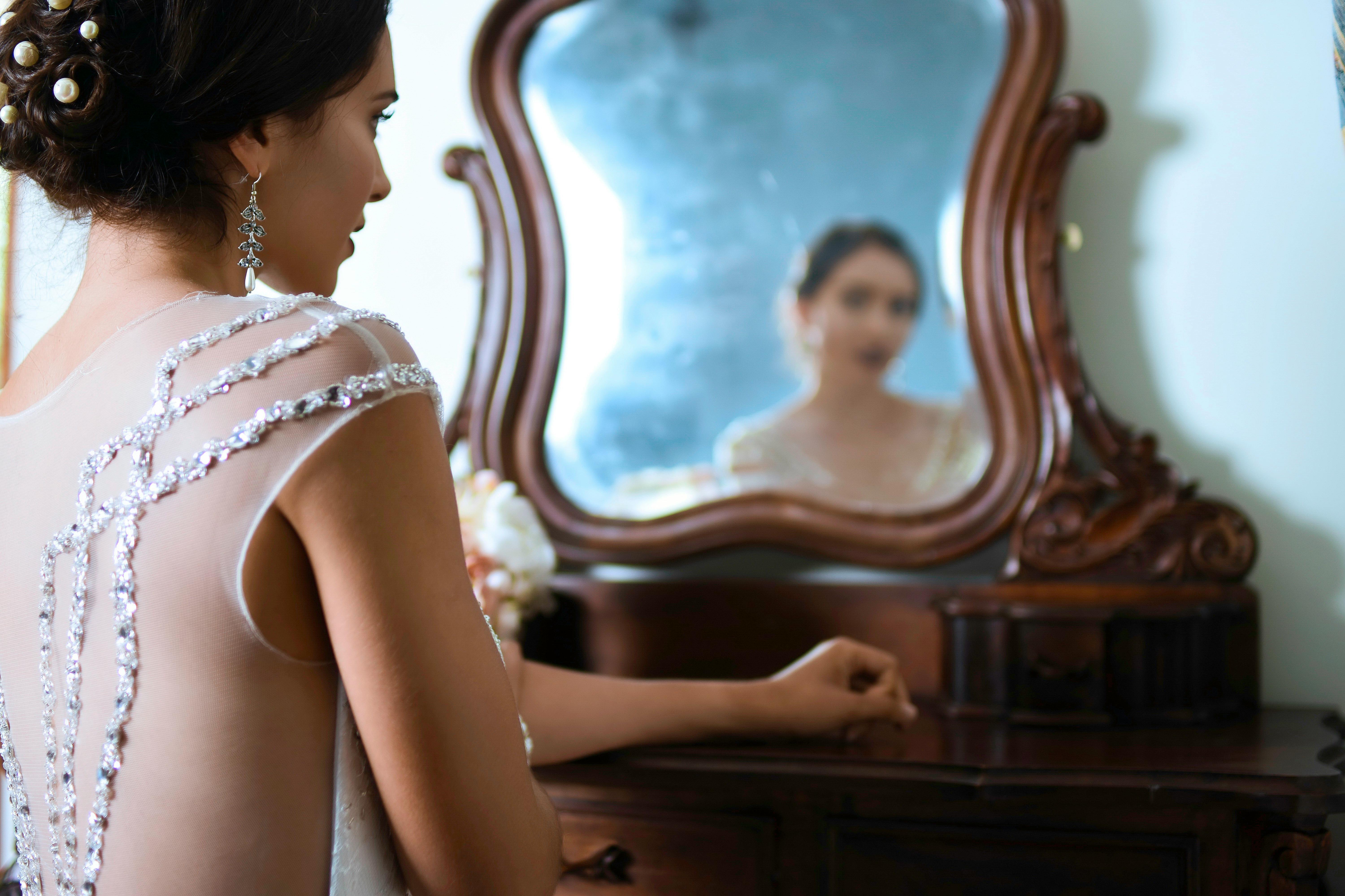 A woman in a wedding dress admires her reflection in the mirror, surrounded by her makeup kit.